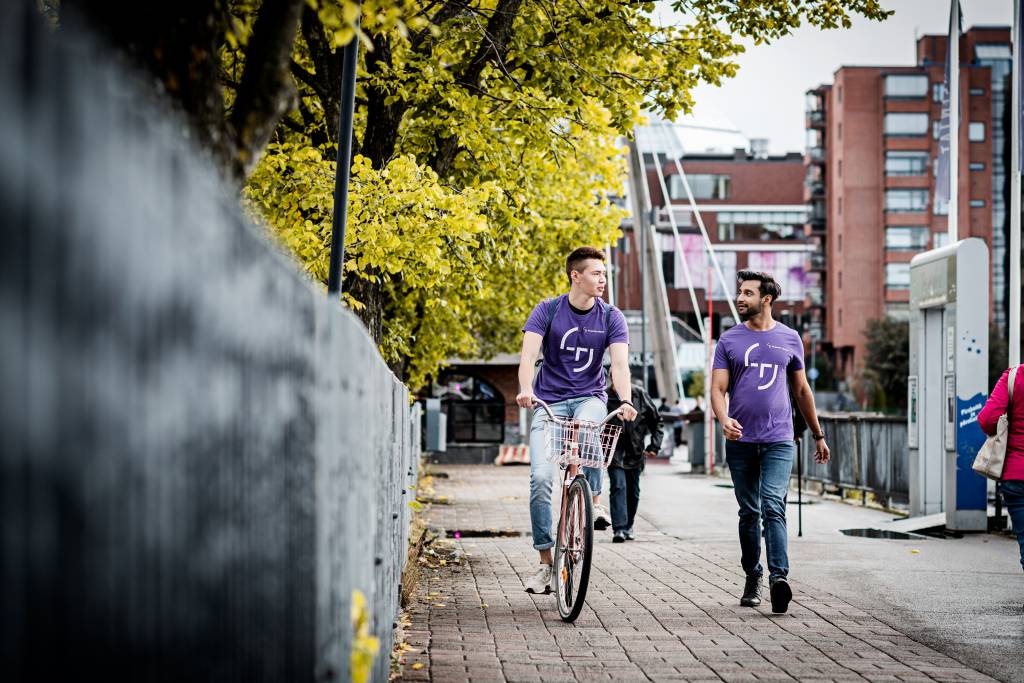 Two student ambassadors wearing purple t-shirts walking and cycling