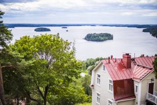 This is a photo of lake pyhäjärvi from the top of the hill in Pispala. In the foreground of the photo is a house with a red roof and a tree.