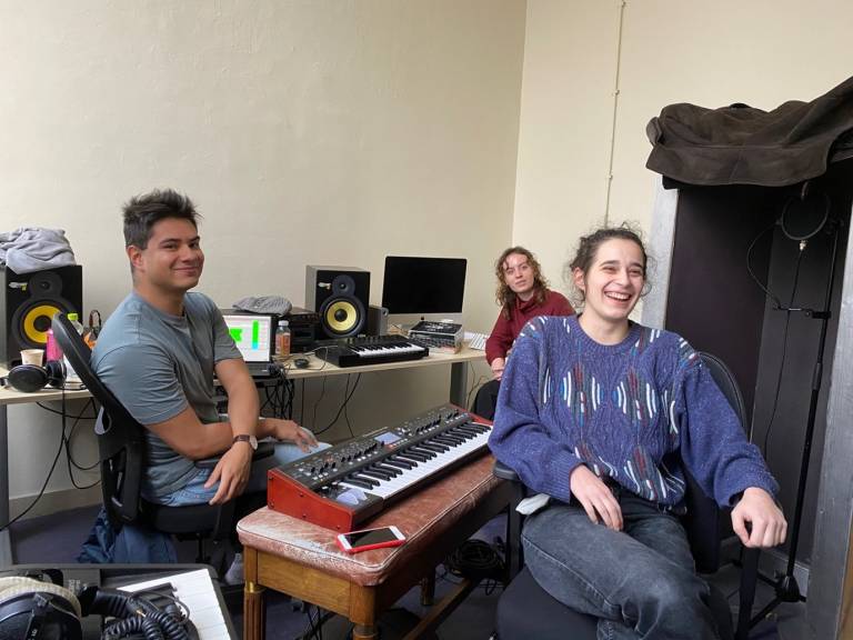 Three students smiling in a room with music instruments.