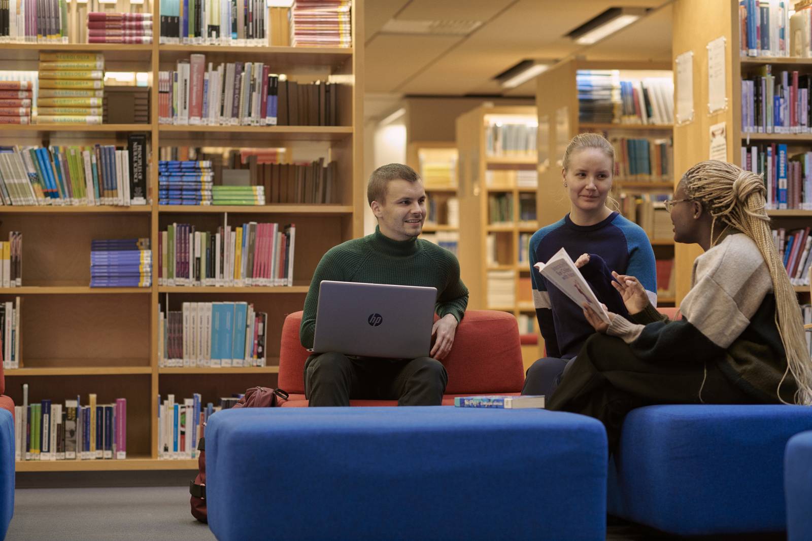 Kolme henkilöä keskustelee kirjastossa.