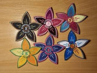 Six flower shaped badges for student overalls from different Symposium-events. Text: Symbosium.